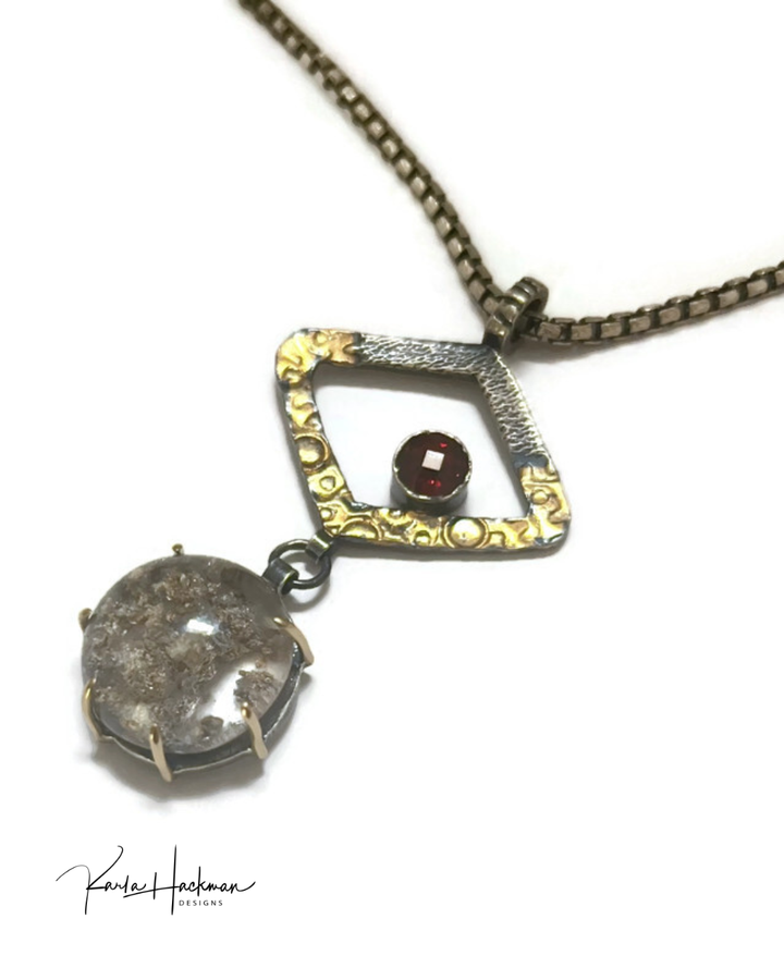 A pendant with two stones, one red and one clear with textured elements, on a white background