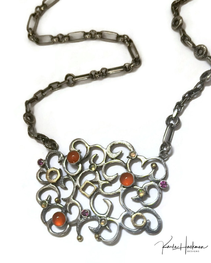 Ornate necklace with a detailed pendant featuring colored stones on a white background.