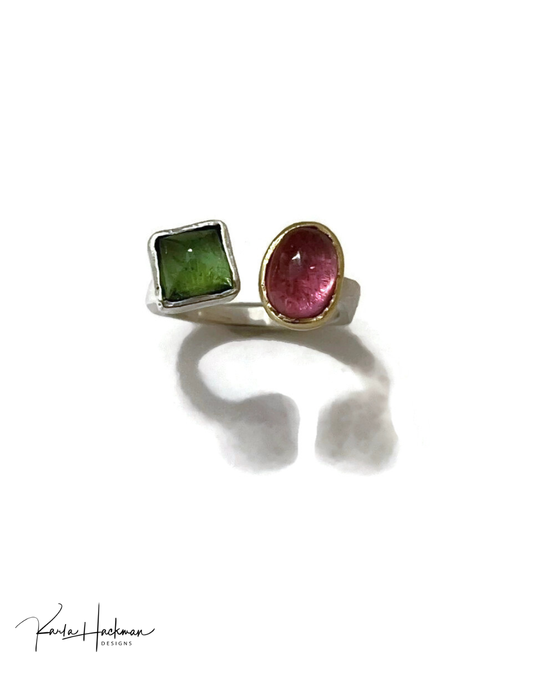 A minimalist two-stone ring set on a white background with a soft shadow. The ring features a square green stone in a silver bezel and an oval pink stone in a gold bezel, both on a silver band.