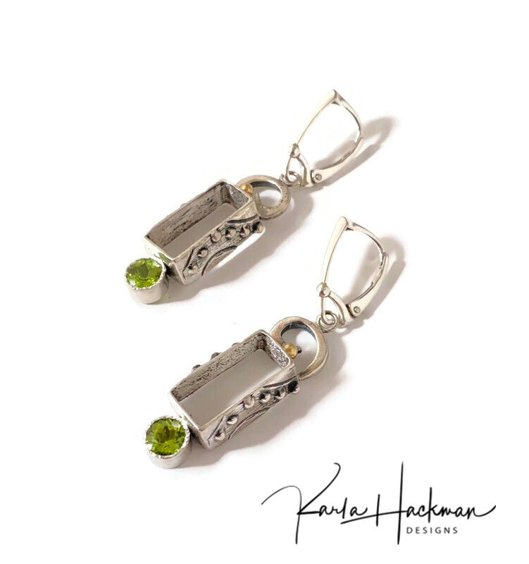 these lovely little, sterling silver, tapered rectangles are adorned on both sides with silver dots and texture. Mounted at the top of the box is a swoosh or spiral shape and an 18 karat gold ball and below hangs a beautiful 6mm peridot gemstone.  Inside of the earrings are given a brushed feeling.